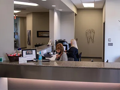 Dental receptionist at front desk in modern clinic office with contemporary décor and lighting.