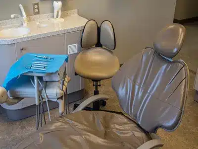 Dental examination chair with overhead light and patient bib in modern clinical operatory room.