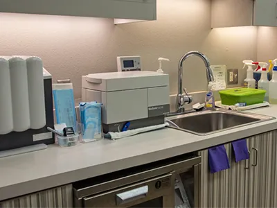 Modern dental laboratory with sterilization equipment, sink, and medical supplies on countertops.