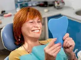 Woman smiling while holding blue dental model in dental office setting.