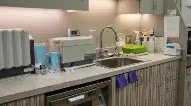 Modern dental office sterilization and preparation area with sink, equipment, and supplies on countertop.