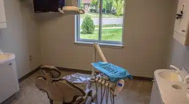 Dental operatory room under renovation with exposed flooring, equipment, and supplies in disarray.